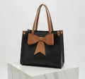 Black handbag with brown handles and large brown bow, displayed on marble surface