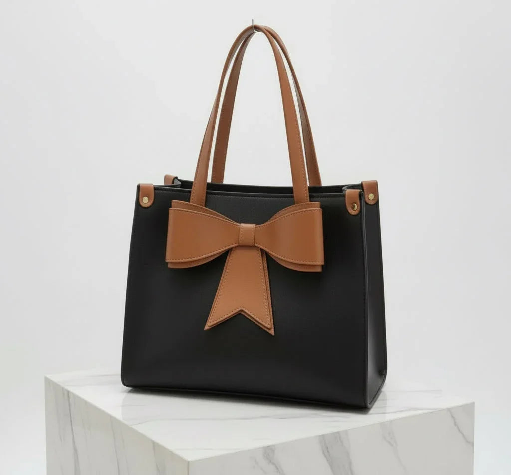Black handbag with brown handles and large brown bow, displayed on marble surface