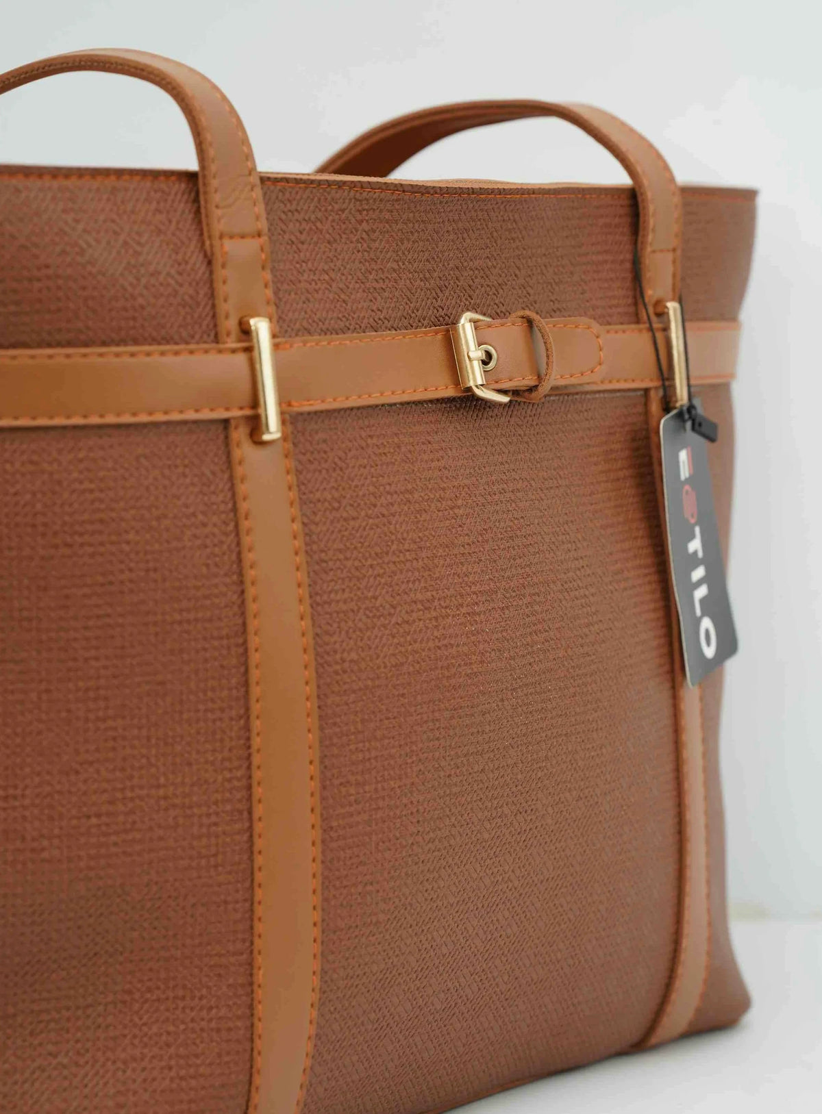 Brown textured tote bag with tan leather straps, gold buckle, and black product tag