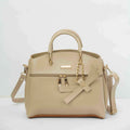 Beige leather handbag with top handles, gold chain, bow accent, and detachable shoulder strap