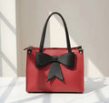 Red handbag with black bow and handles displayed on a white surface in natural light