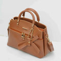 Tan leather handbag with gold chain accents, front zipper pocket, and bow detail