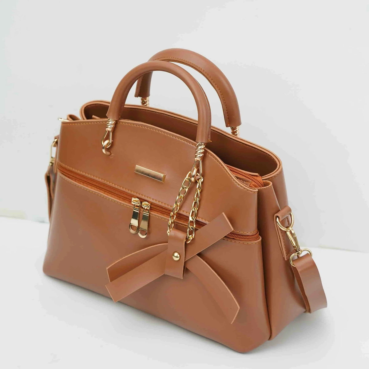 Tan leather handbag with gold chain accents, front zipper pocket, and bow detail