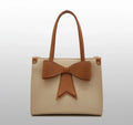 Beige tote bag with brown handles and a large brown bow on the front, minimalist style