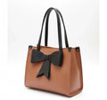 Brown tote handbag with black handles and a large black bow, fashion accessory