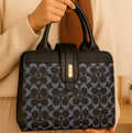 Woman holding a black and blue patterned handbag with gold accents in a cozy indoor setting