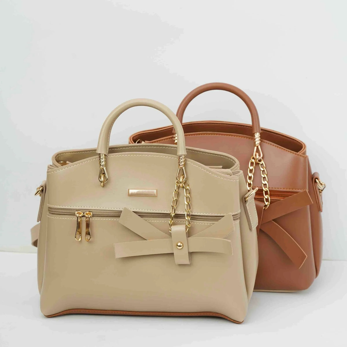 Beige and brown handbags with gold chain handles and bow accents on a white background