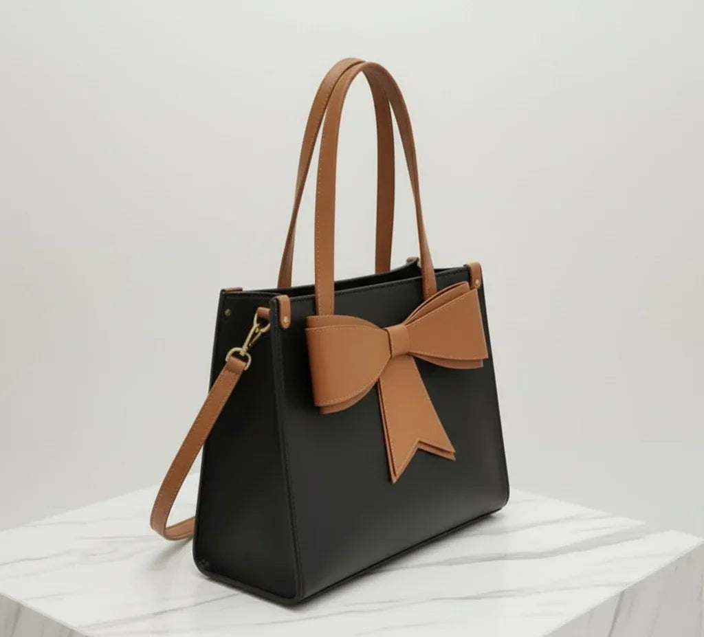 Black tote bag with brown bow detail, double handles, and shoulder strap on marble surface