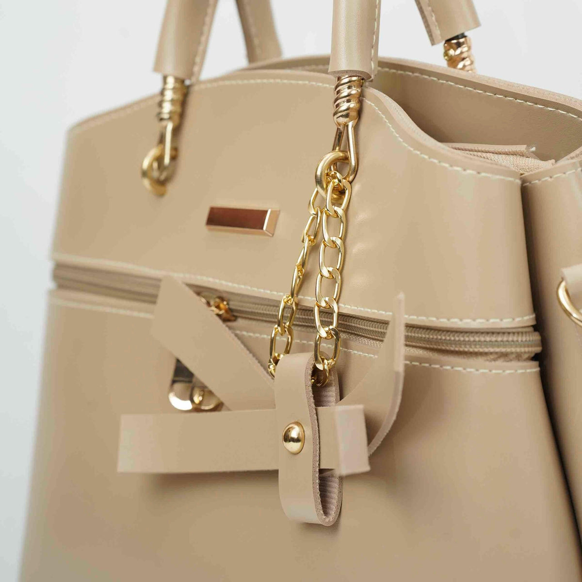 Beige handbag with gold chain detail, zipper, and modern hardware, close-up view